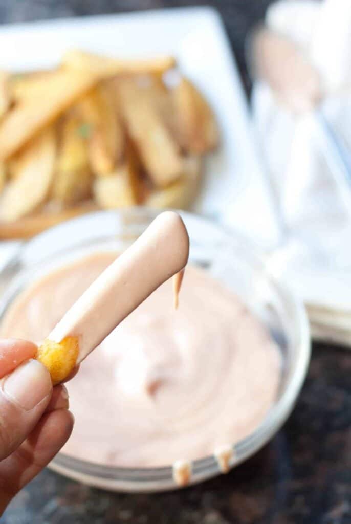 a hand holding a fry dipped in fry sauce.