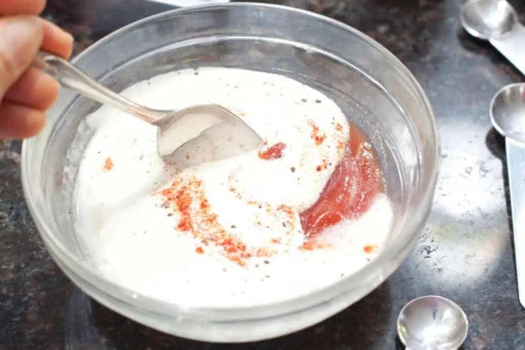 a bowl of mayo with ketchup being mixed with a spoon.