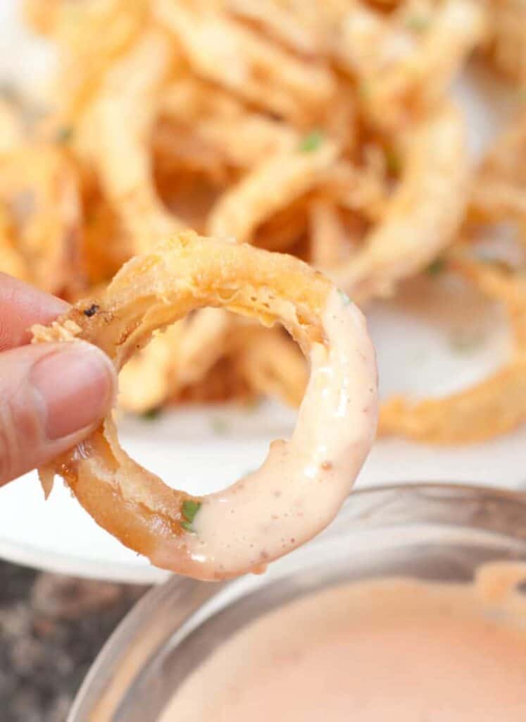 a hand holding an onion ring dipped in fry sauce.