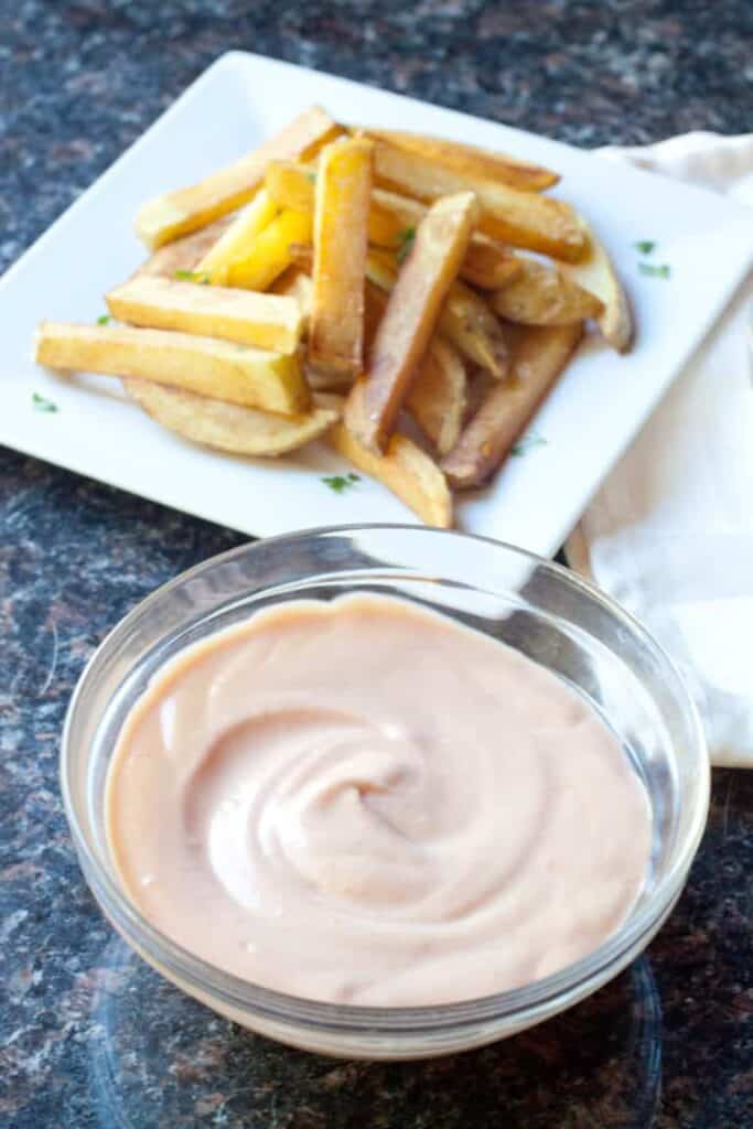 a bowl of fry sauce in front of a plate of fries.