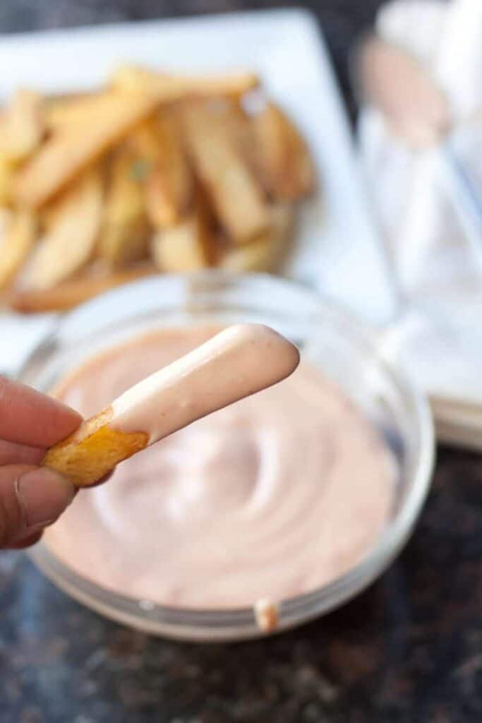 a hand holding a fry dipped in fry sauce.