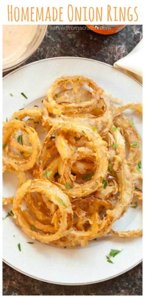 an overhead of a plate of onion ringsa plate of onion rings and a hand dipping onion ring in sauce with Pinterest pin text.