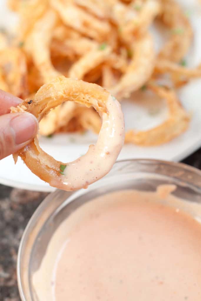 crispy onion ring dipped in a bowl of fry sauce.