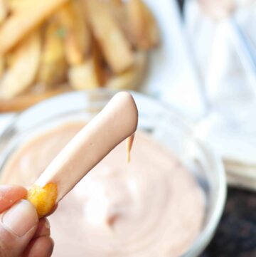 a hand holding a french fry dipped in sauce
