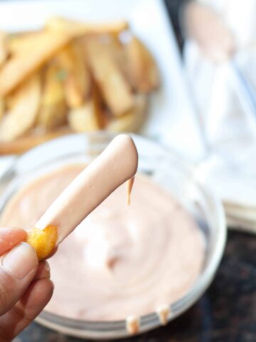 a hand holding a french fry dipped in sauce