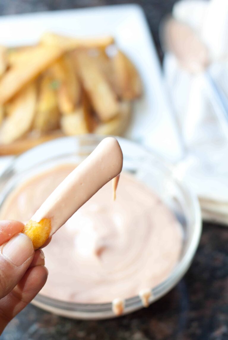 a hand holding a french fry dipped in sauce