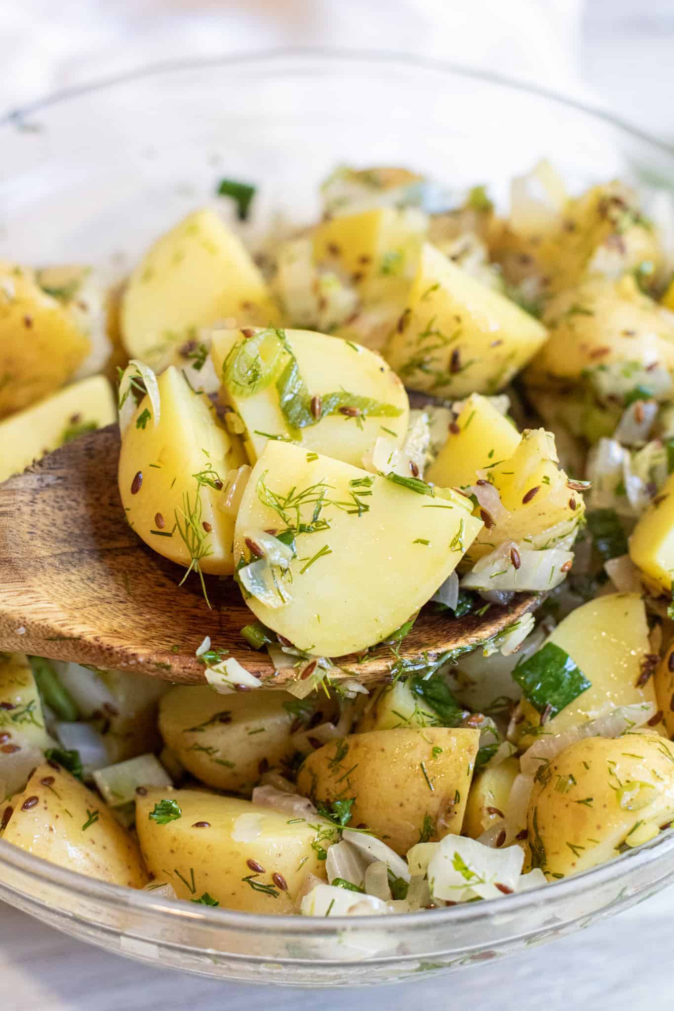 a wooden spoon holding up some potato salad with dill.
