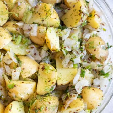 a bowl of yellow potato salad with seeds, onions, and dill.