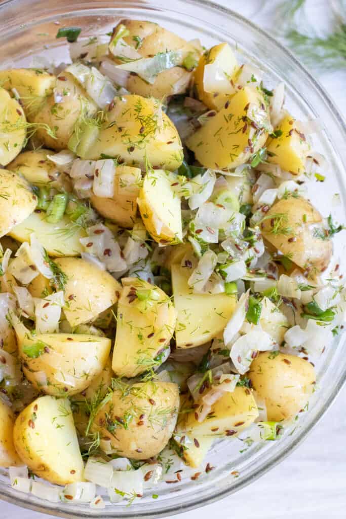 a bowl of yellow potato salad with seeds, onions, and dill.