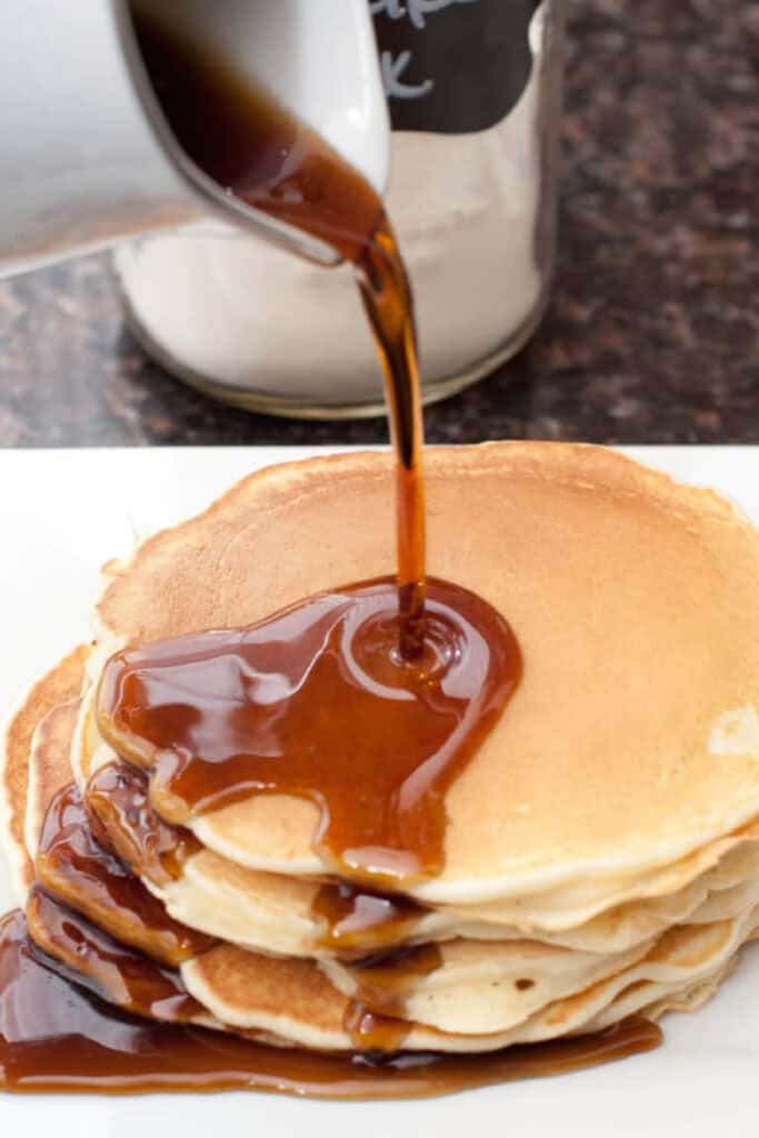 syrup being poured on a stack of pancakes.