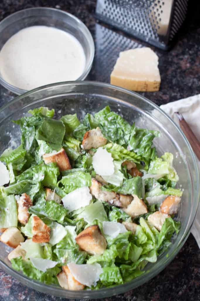 a large bowl of Caesar salad mixed with dressing.