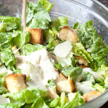 a large bowl of salad with dressing being poured in.