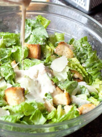 a large bowl of salad with dressing being poured in.