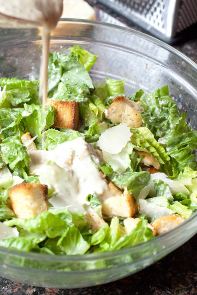 Caesar dressing being poured into a bowl of salad.