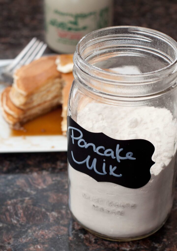 a jar of homemade pancake mix with cooked pancakes in the background