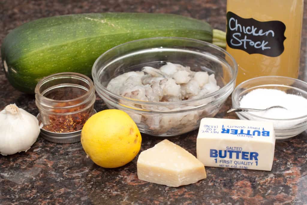 zucchini, shrimp, stock, parmesan, spices, butter, garlic on a counter.