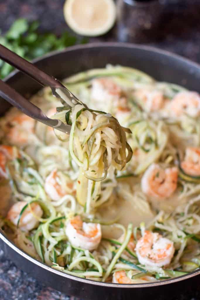 tongs holding up cooked zoodles.