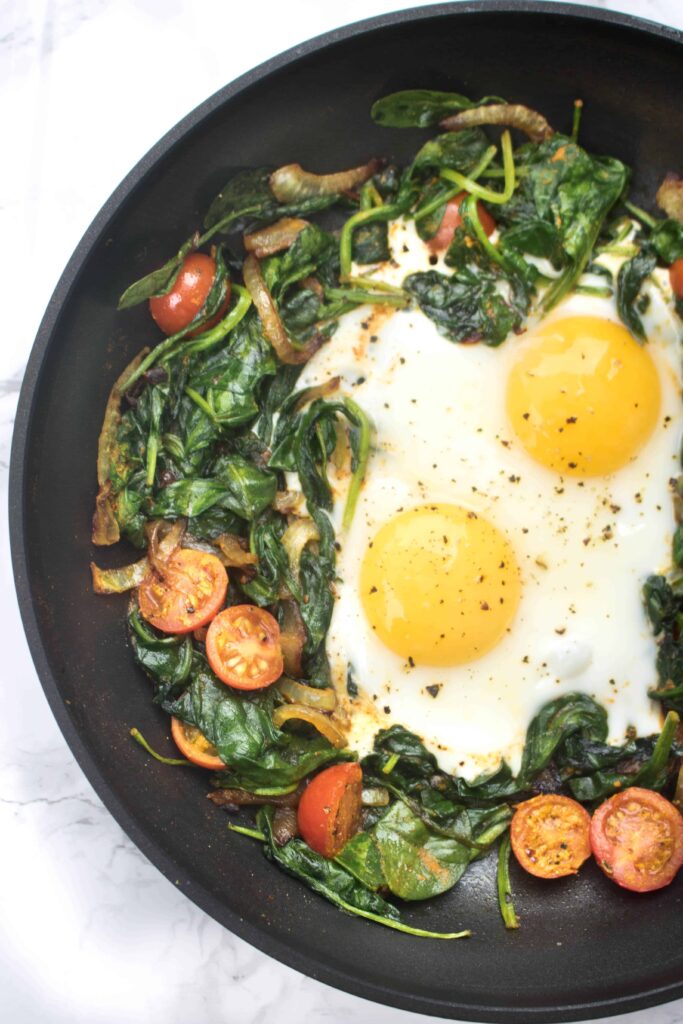 a pan with sauteed spinach, tomatoes, onions, and eggs