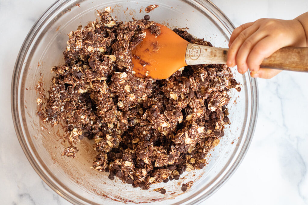 toddler hand mixing an oat, chocolate, dough.