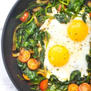 a pan with sauteed spinach, tomatoes, onions, and eggs