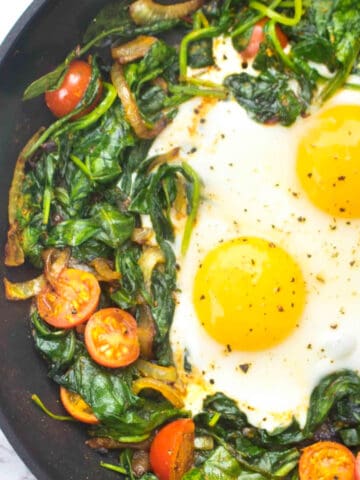 a pan with sauteed spinach, tomatoes, onions, and eggs