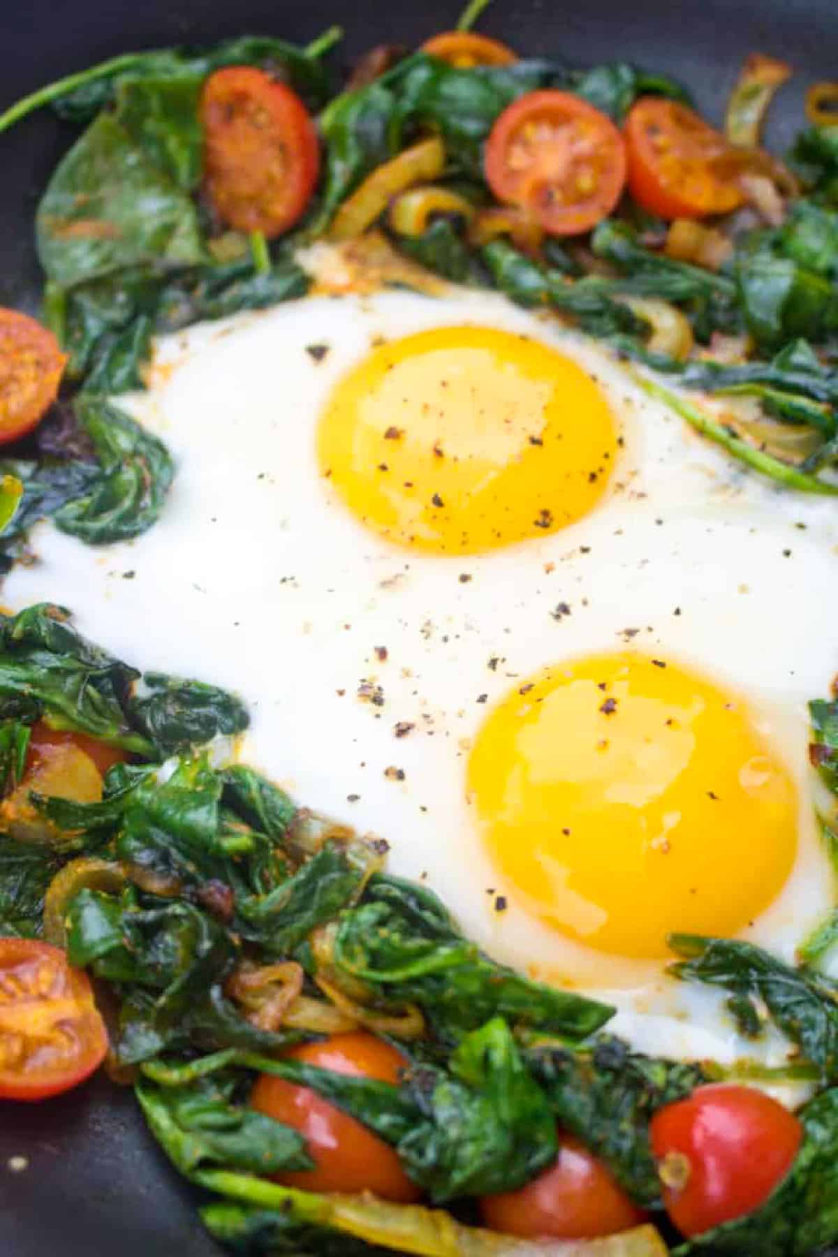 a pan with sauteed spinach, tomatoes, onions, and eggs