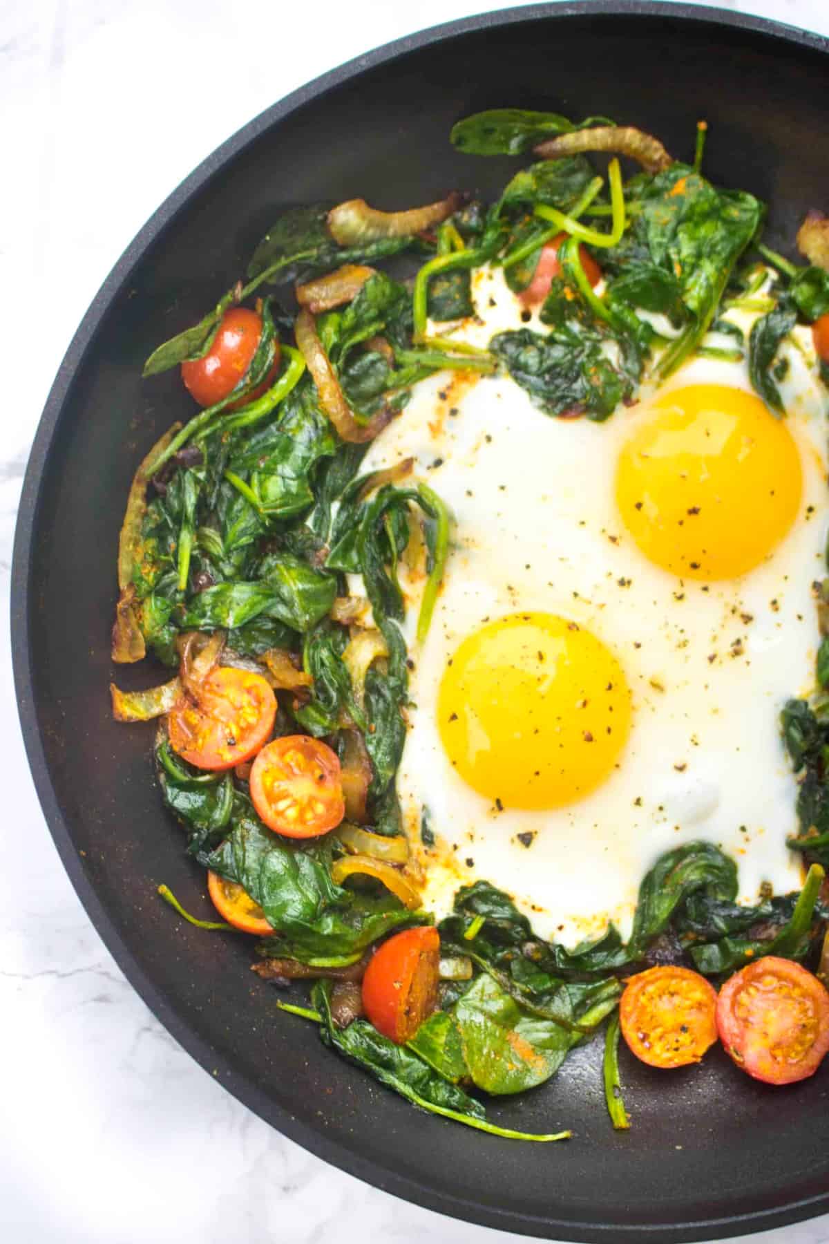 a pan with sauteed spinach, tomatoes, onions, and eggs