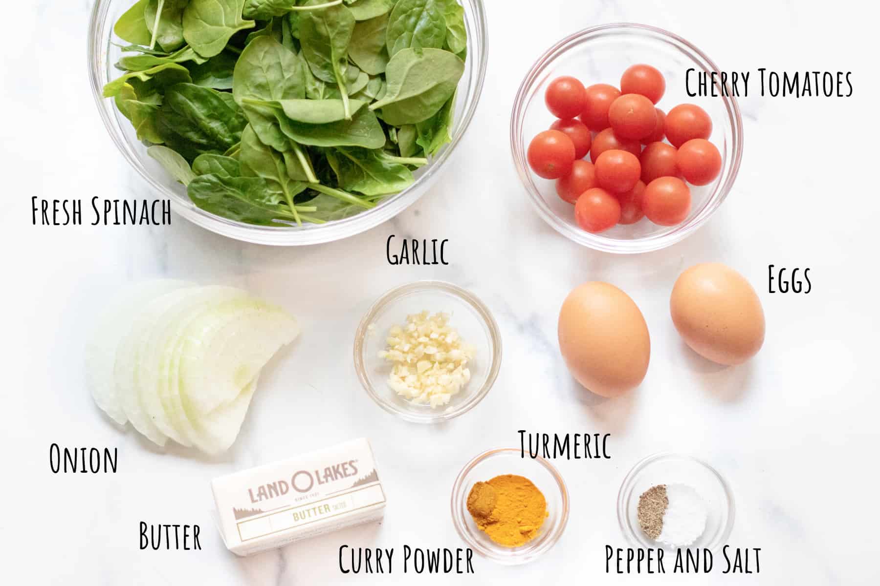 bowl of spinach, tomatoes, sliced onion, eggs, and spices and garlic.