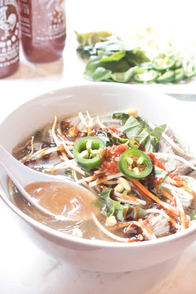 a bowl of beef pho with a spoon ladeling broth