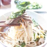 a bowl of beef pho with chopsticks holding a bite up