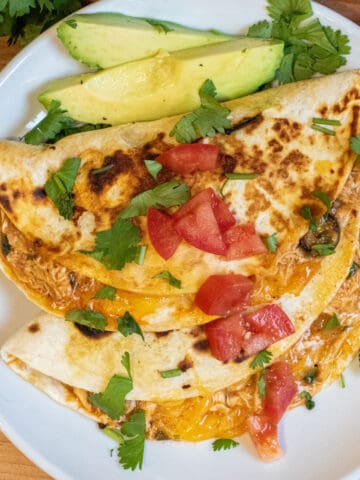 an overhead of tacos covered with cilantro and tomatoes on a plate with sliced avocado.