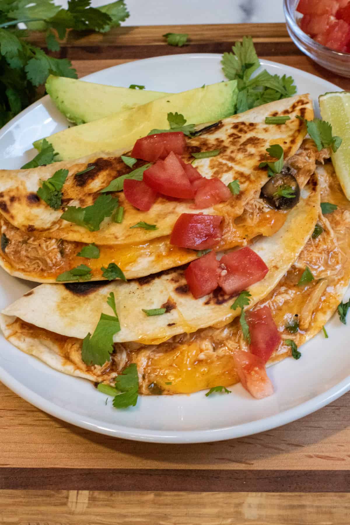 an overhead of tacos covered with cilantro and tomatoes on a plate with sliced avocado.