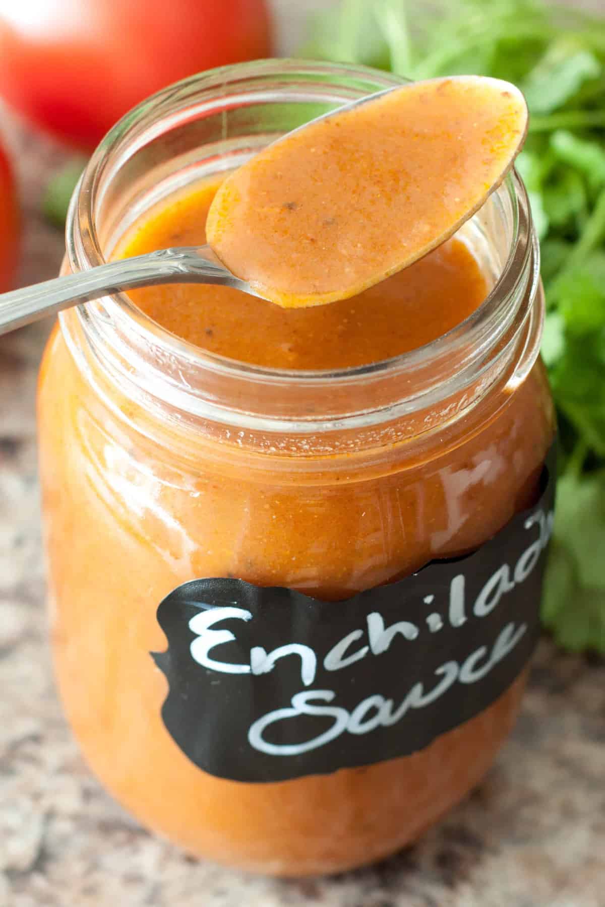 an open jar of enchilada sauce in a mason jar with a spoon.