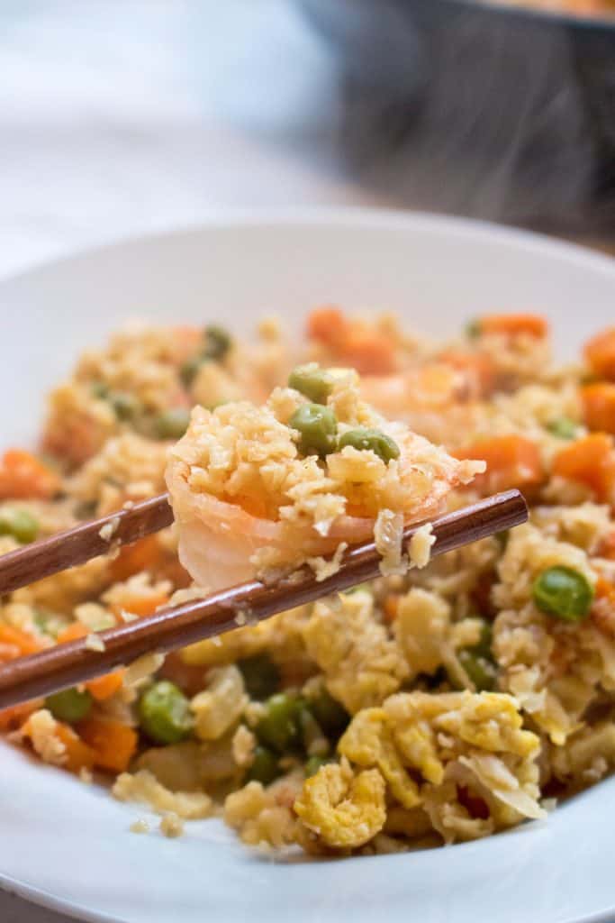 cooked cauliflower shrimp fried rice in a bowl held by chopsticks.