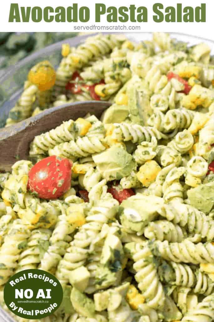 green pasta salad with tomatoes and corn with a wooden spoon in it with Pinterest pin text and NO AI sticker.