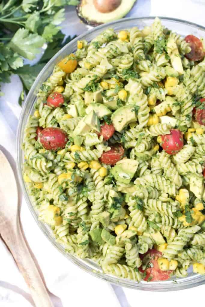 an overhead of a green pasta salad with tomatoes, corn, and avocados.