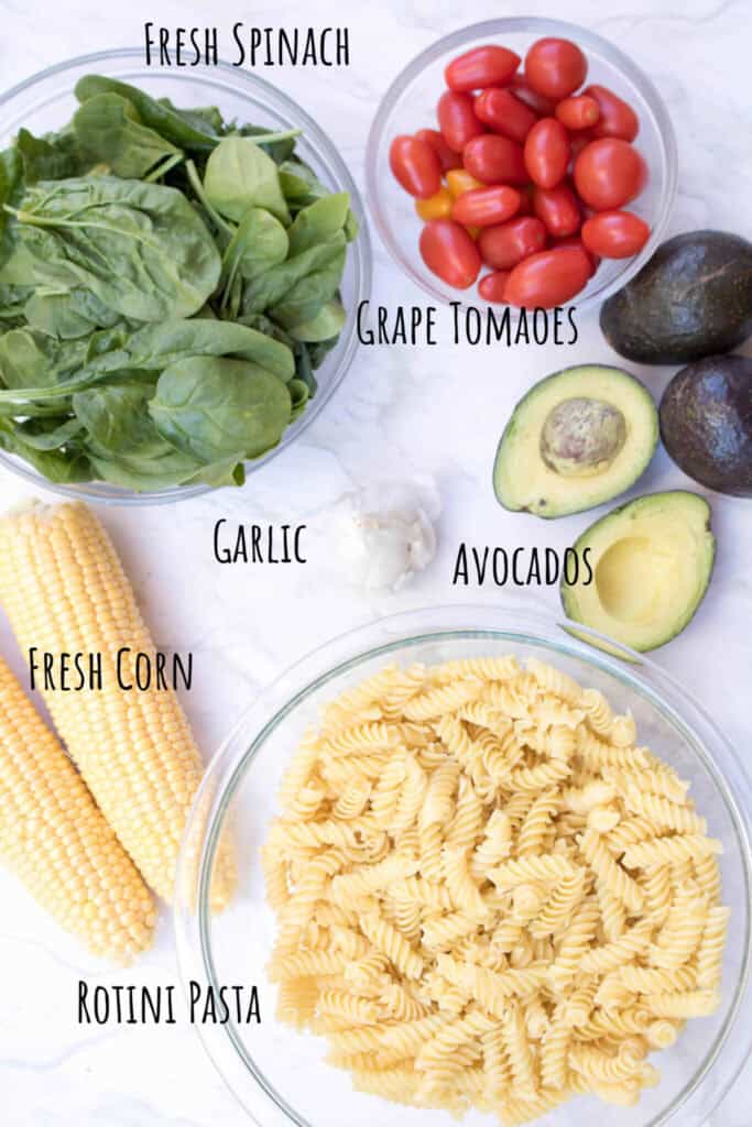 a bowl of pasta, ears of corn, tomatoes, spinach, and avocados labeled.