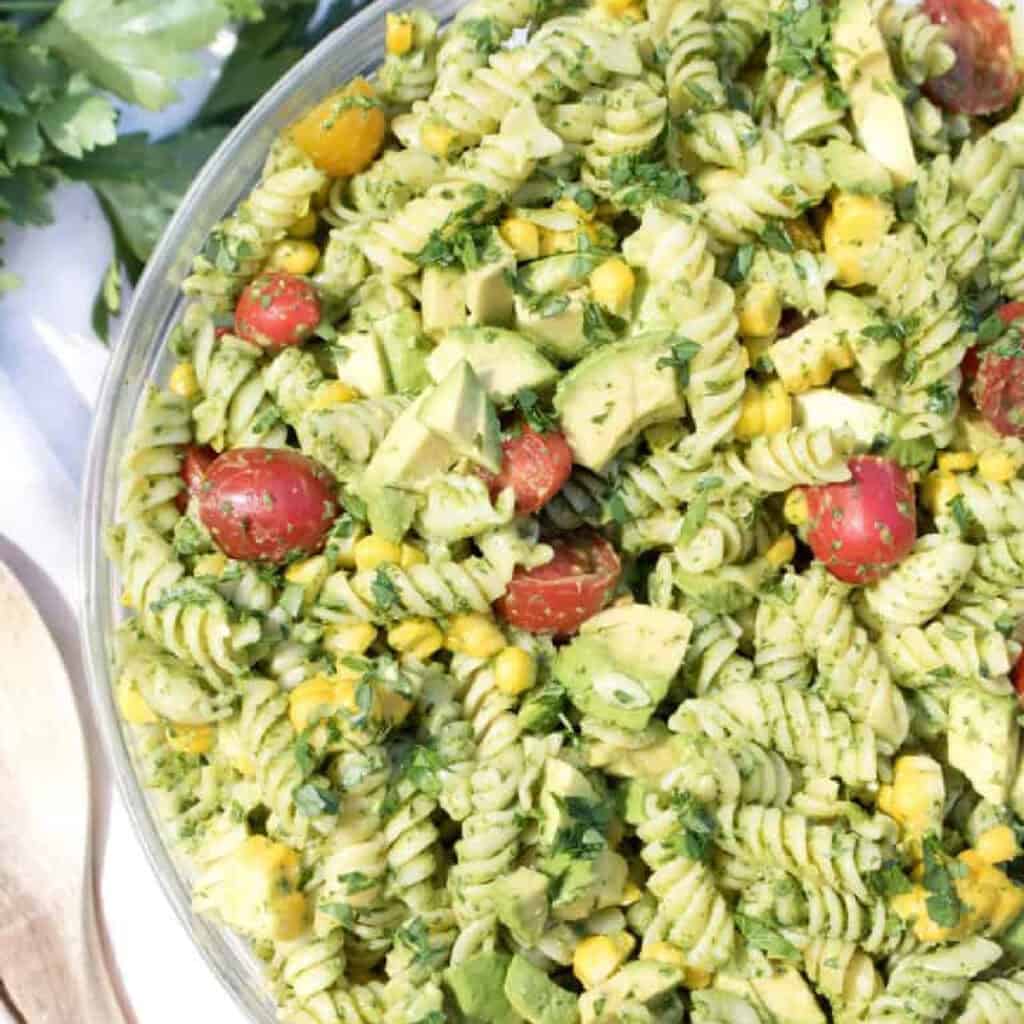 an overhead of a green pasta salad with tomatoes, corn, and avocados.
