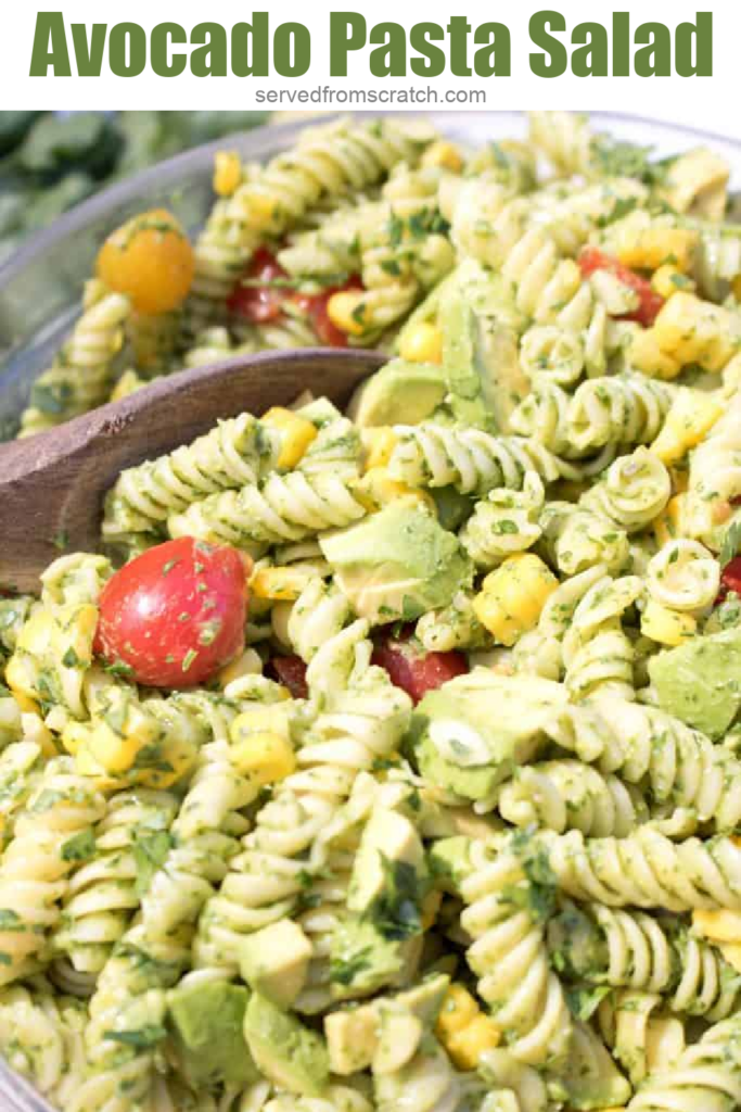 wooden spoon in a large bowl of green pasta salad with Pinterest pin text.