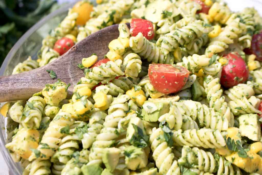 wooden spoon in a large bowl of green pasta salad.