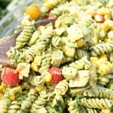 wooden spoon in a large bowl of green pasta salad.