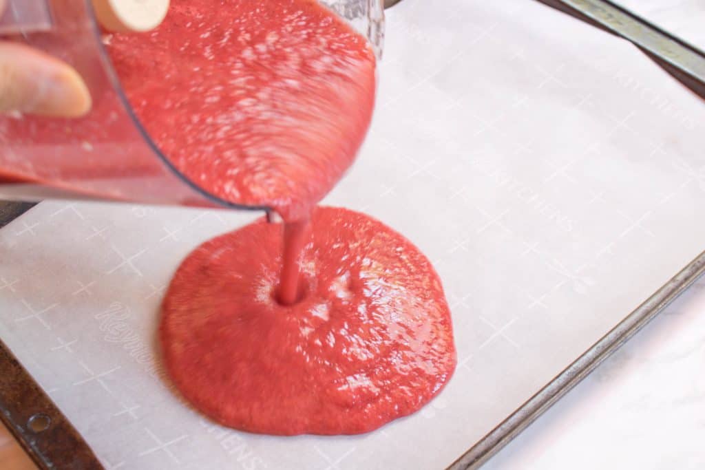 pureed strawberry mixture being poured from food processor on to parchment lined trays.
