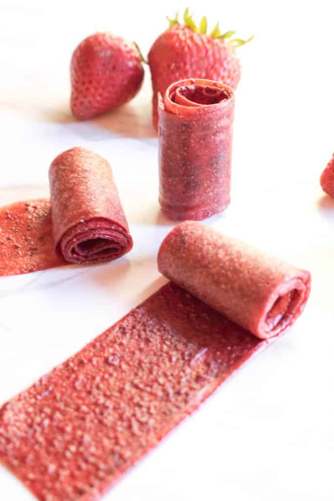 homemade strawberry fruit roll ups, rolled up and unrolled with fresh strawberries.