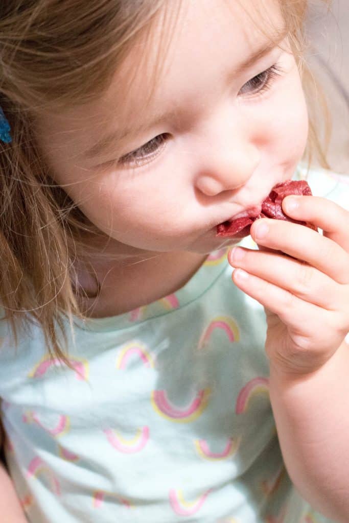 Little girl putting strawberry fruit roll up in her mouth.