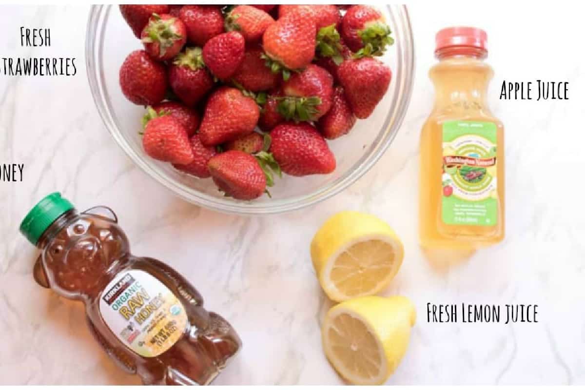 a bowl of strawberries, honey, juice, and lemon halved.
