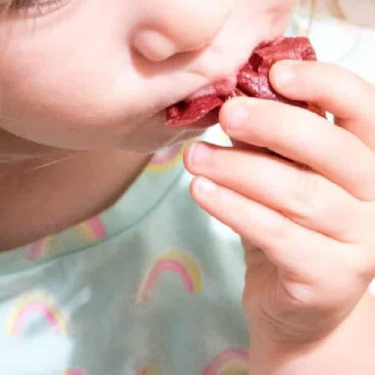 a little girl eating a mashed up fruit roll up.