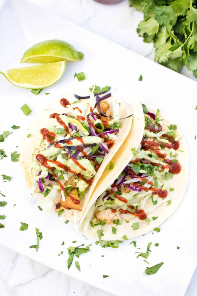 a plate with an open taco with chicken, sriracha, avocado sauce, cabbage, and cilantro.