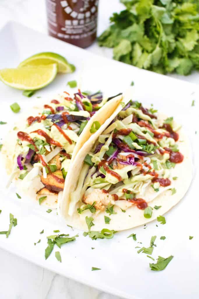 a plate with an open taco with chicken, sriracha, avocado sauce, cabbage, and cilantro.