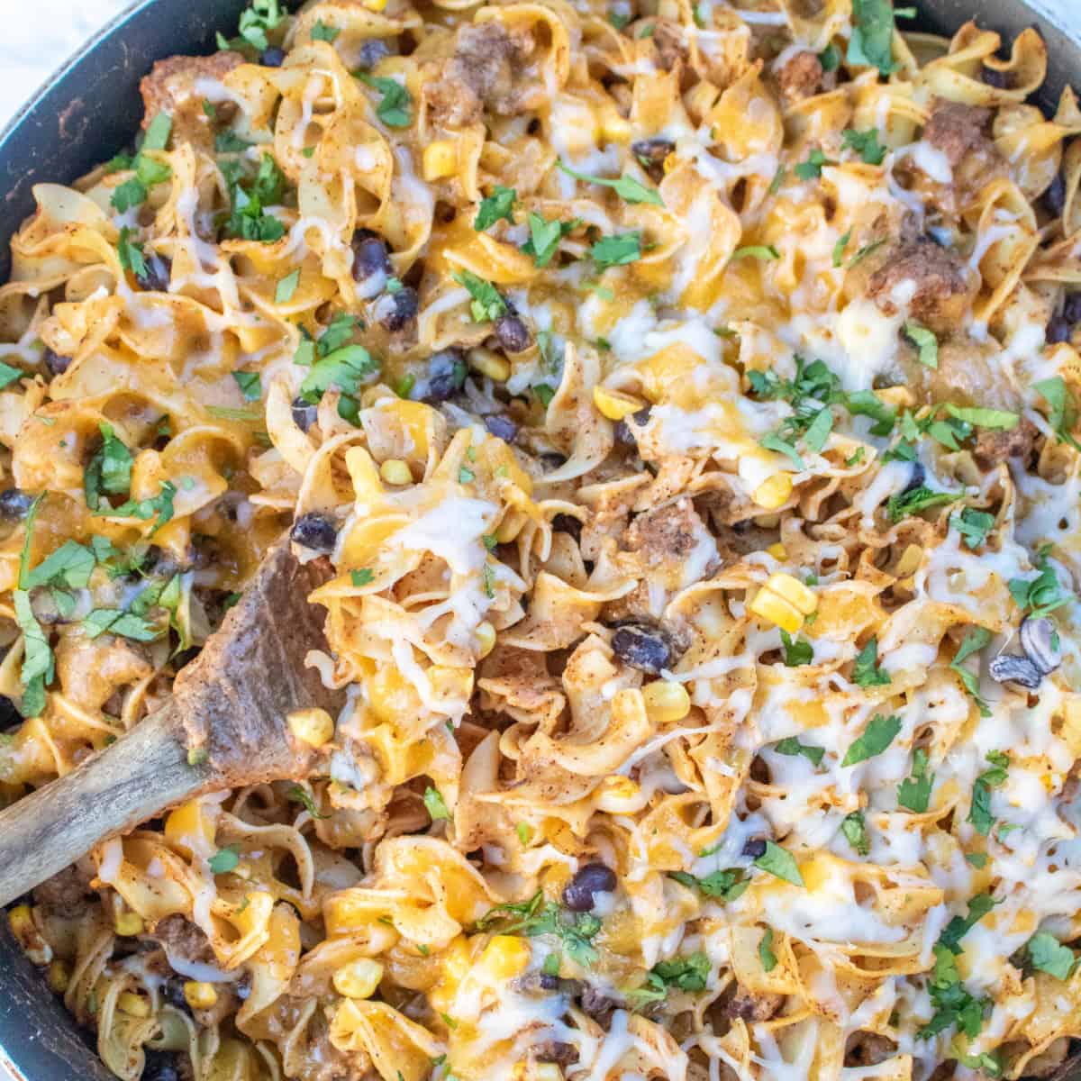 an overhead of a cheesy pasta skillet with beef and beans and a wooden spoon.