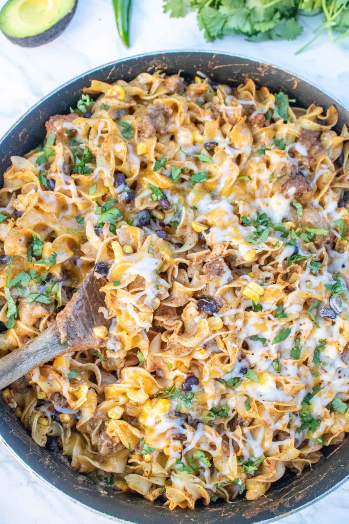 an overhead of a cheesy pasta skillet with beef and beans and a wooden spoon.